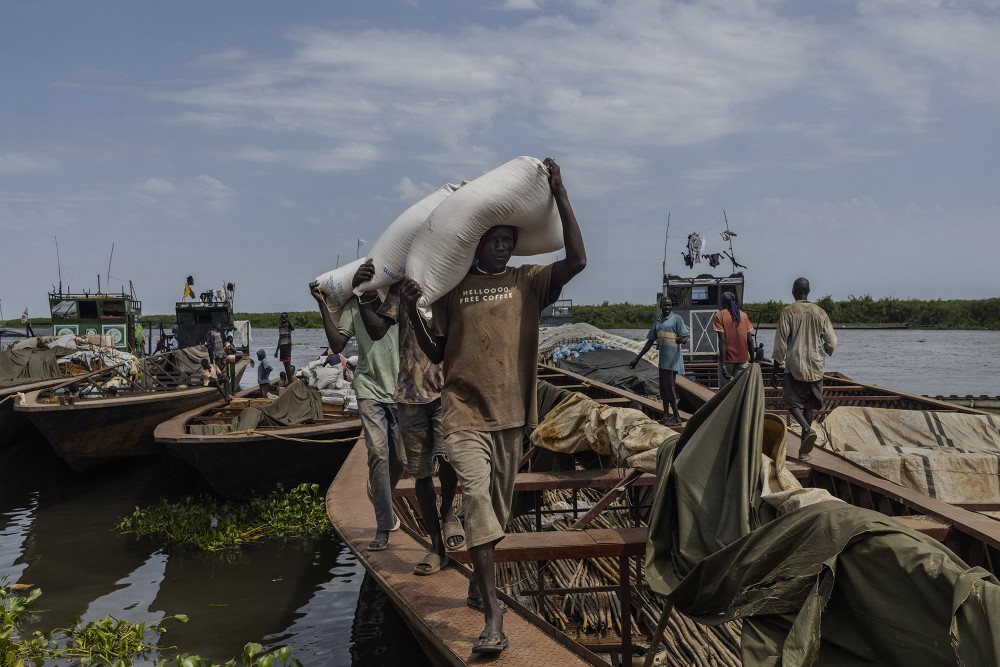 Workers unload bags of food that arrived at Adok Port on the banks of the White Nile, on November 19, 2022.A large section of the White Nile flows through South Sudan and the country has access to approximately 1400 km of navigable waterways which stretch from the north to the south of the country. Although navigable year-round, water levels fluctuate during the rainy and dry seasons. In some areas, this results in the reduced carrying capacity of barges and difficulty in transporting goods. As a result, the price of goods continues to increase affecting the cost of living.